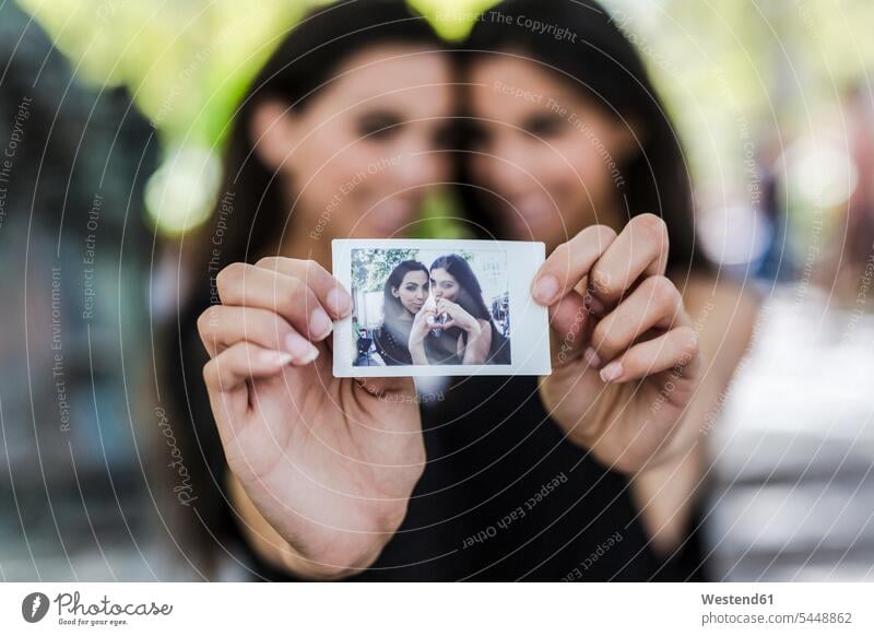 Zwei Zwillingsschwestern halten ein Sofortfoto von sich Foto Fotos Schwester Schwestern Freundinnen Bild Bildnis Bilder Geschwister Familie Familien Mensch