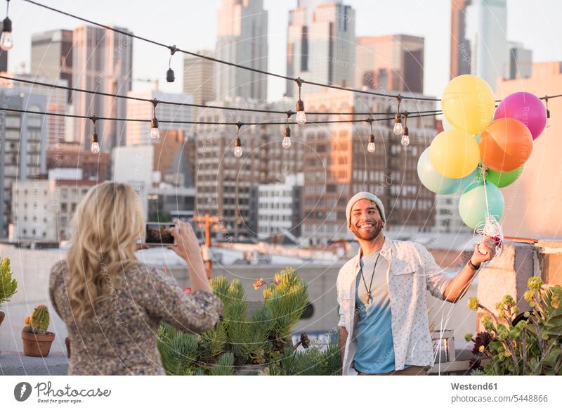 Junges Paar mit Luftballons steht auf der Dachterrasse und benutzt ein Smartphone glücklich Glück glücklich sein glücklichsein Ballons Luftballone iPhone