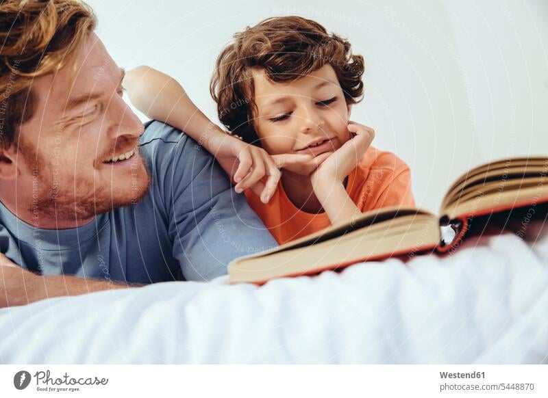 Vater und Sohn lesen Buch im Bett Bücher liegen liegend liegt Papas Väter Vati Vatis Papis entspannt entspanntheit relaxt Lektüre Söhne Betten Eltern Familie