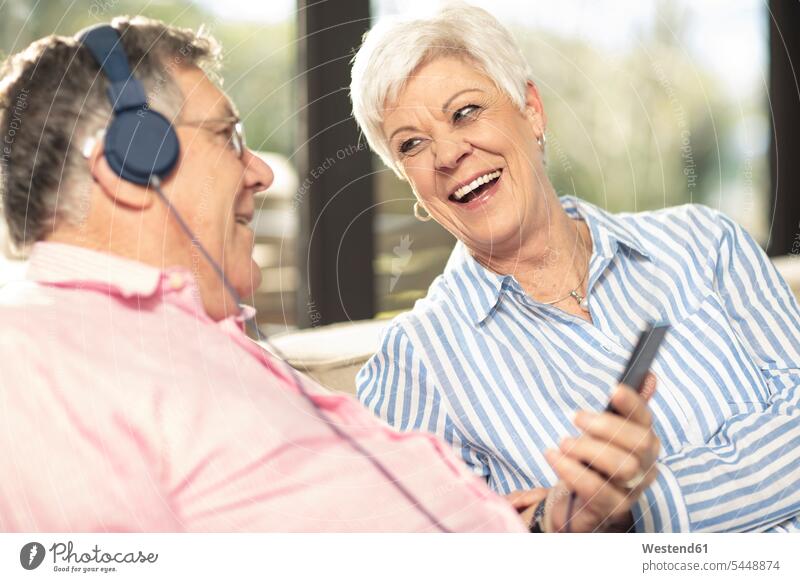 Glückliches älteres Ehepaar mit Handy und Kopfhörern auf der Couch zu Hause Kopfhoerer glücklich glücklich sein glücklichsein Paar Pärchen Paare Partnerschaft