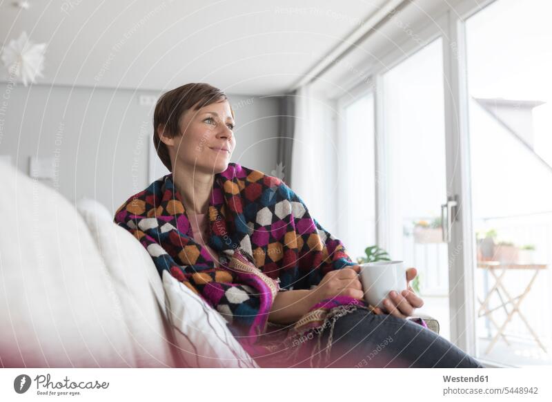 Porträt einer Frau, die sich bei einer Tasse Kaffee zu Hause entspannt weiblich Frauen Sofa Couches Liege Sofas Wohnzimmer Wohnraum Wohnung Wohnen Wohnräume