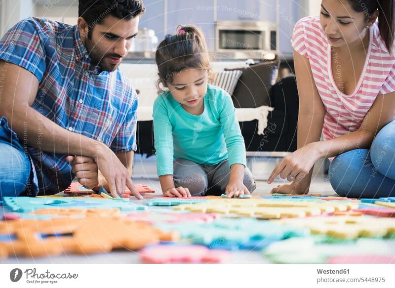 Glückliche Familie sitzt auf dem Boden und spielt mit der Tochter Familien lernen Zuhause zu Hause daheim Puzzle Puzzlespiel sitzen sitzend spielen Böden Boeden