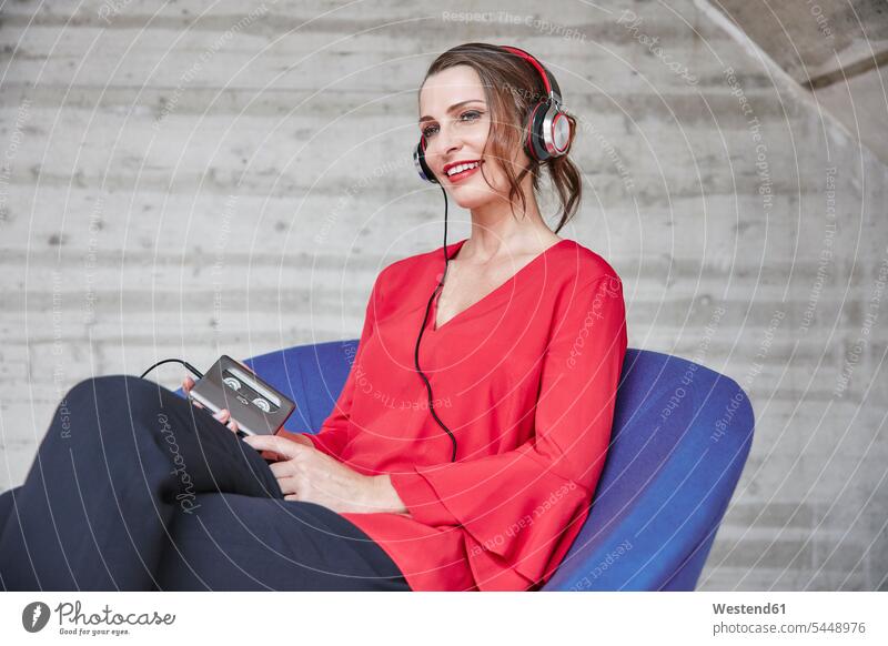 Lächelnde Frau sitzt auf Stuhl und hört Musik vom Walkman sitzen sitzend lächeln Kopfhörer Kopfhoerer weiblich Frauen hören hoeren Erwachsener erwachsen Mensch