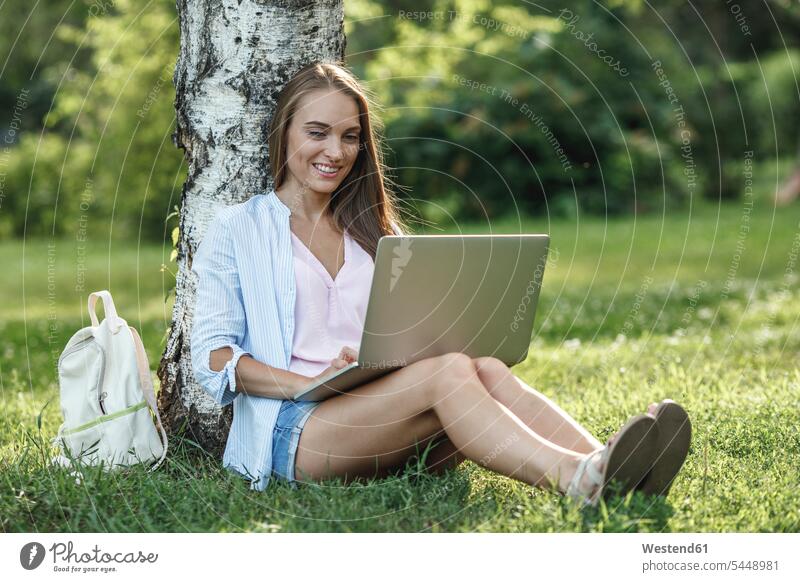 Lächelnde junge Frau mit Laptop auf einer Wiese lächeln Park Parkanlagen Parks weiblich Frauen Notebook Laptops Notebooks Erwachsener erwachsen Mensch Menschen