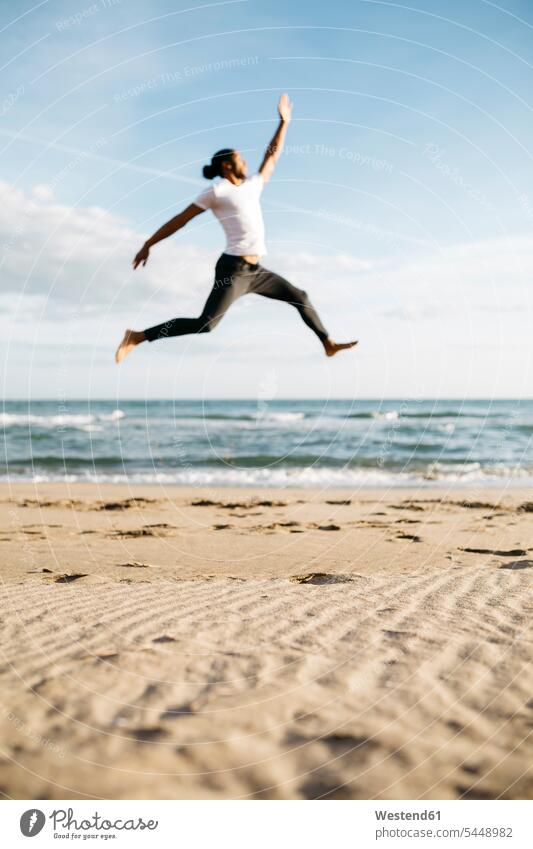 Junger Mann springt am Strand in die Luft Beach Straende Strände Beaches Männer männlich Erwachsener erwachsen Mensch Menschen Leute People Personen Sand sandig