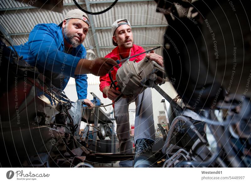 Mechaniker reparieren Auto in der Werkstatt Reparatur besprechen diskutieren Besprechung restaurieren arbeiten Arbeit Kollegen Arbeitskollegen Werkstätte
