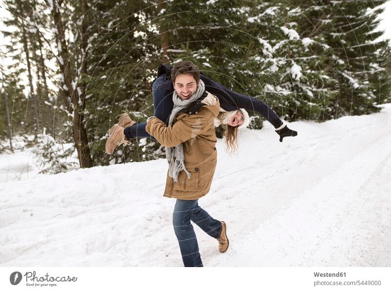Glückliches junges Paar amüsiert sich in schneebedeckter Winterlandschaft Pärchen Paare Partnerschaft Mensch Menschen Leute People Personen verspielt