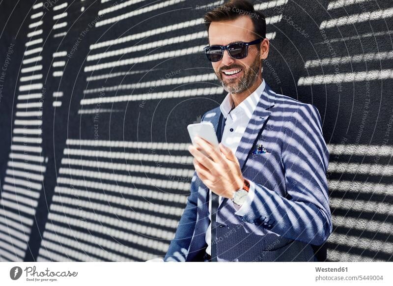 Geschäftsmann mit Sonnenbrille benutzt Telefon in der Nähe einer Betonwand lächeln Businessmann Businessmänner Geschäftsmänner Handy Mobiltelefon Handies Handys