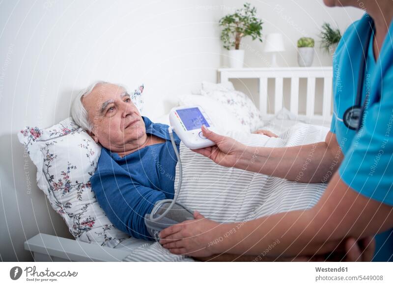 Gereatrische Krankenschwester, die den Blutdruck eines im Bett liegenden Patienten misst Betreuung betreuen Altenpflege liegt Behandlung Krankenbehandlung