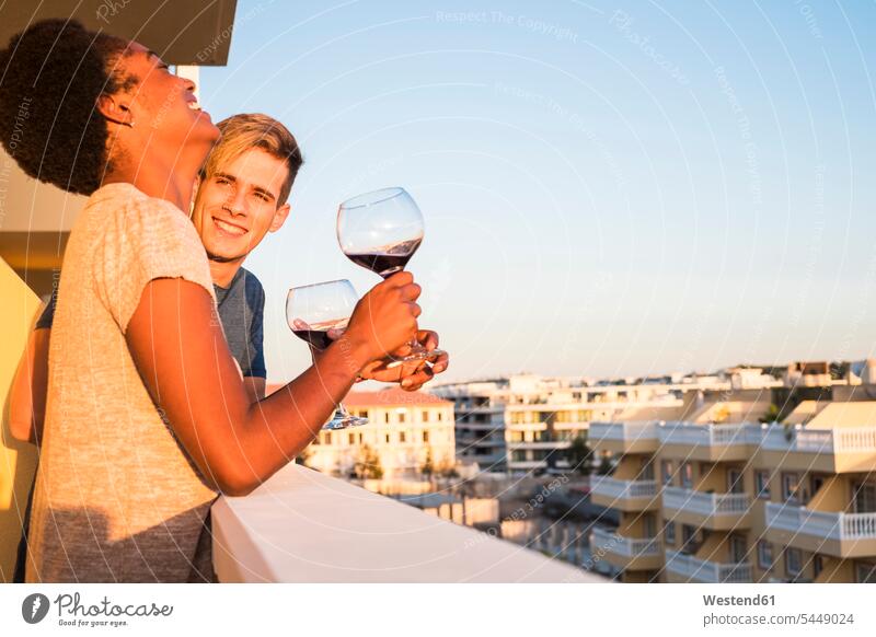 Glückliches junges Paar trinkt Wein auf dem Balkon Balkone trinken Weinglas Weingläser Pärchen Paare Partnerschaft entspannt entspanntheit relaxt Weine Glas