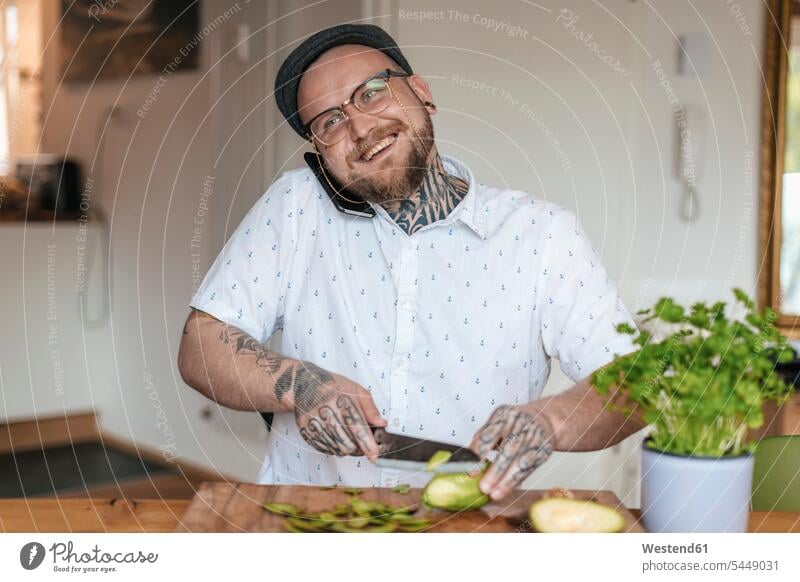 Lächelnder Mann am Telefon beim Gemüseschneiden in der Küche telefonieren anrufen Anruf telephonieren abschneiden kleinschneiden Männer männlich