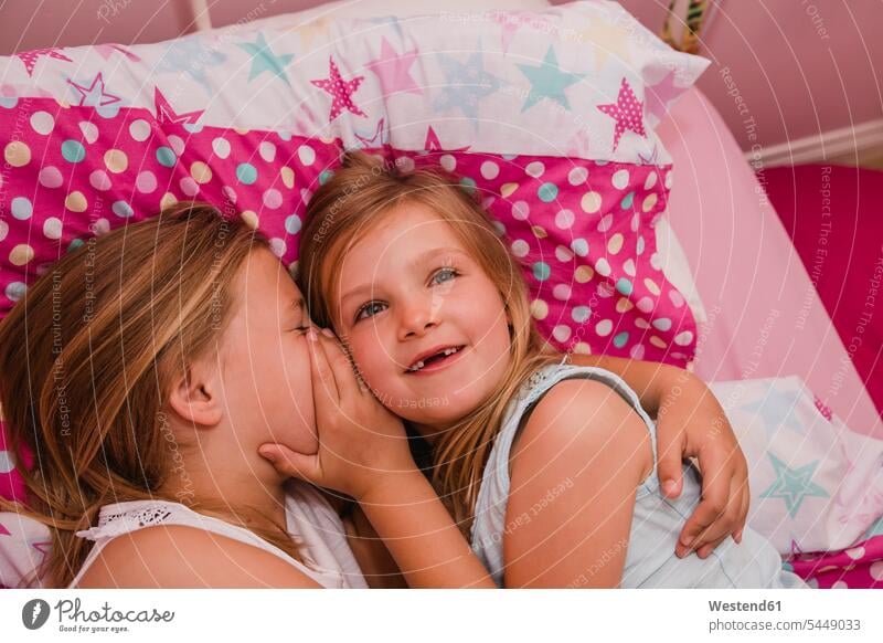 Mädchen, das mit seiner kleinen Schwester im Bett liegt und ein Geheimnis verrät Schwestern weiblich Betten Portrait Porträts Portraits Geschwister Familie