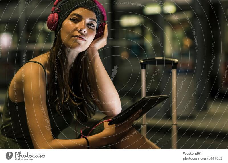 Porträt einer jungen Frau mit Kopfhörer und Tablette, die nachts am Bahnhof wartet weiblich Frauen Kopfhoerer Erwachsener erwachsen Mensch Menschen Leute People