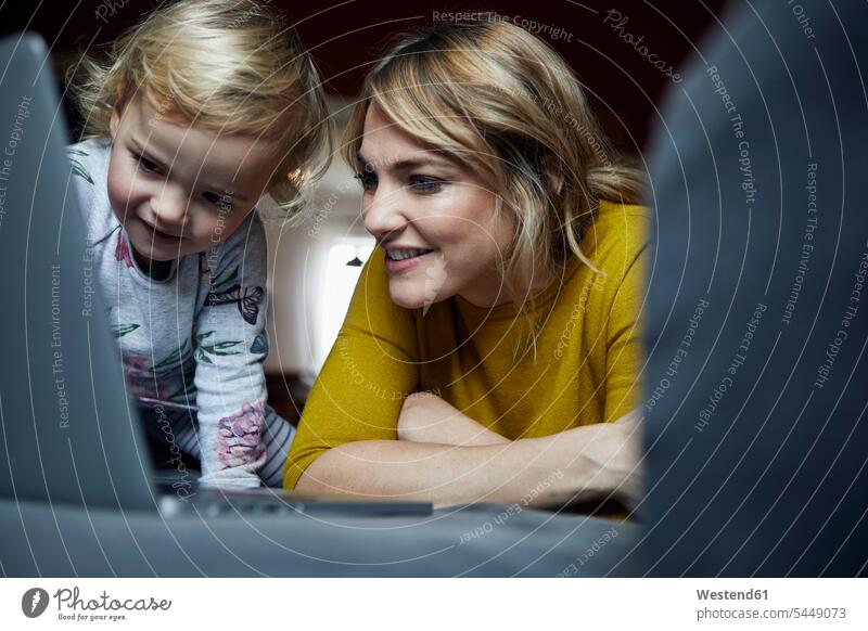 Portrait von Mutter und kleiner Tochter, die zu Hause auf den Laptop schauen Zuhause daheim Mami Mutti Mütter Mama ansehen Töchter Notebook Laptops Notebooks