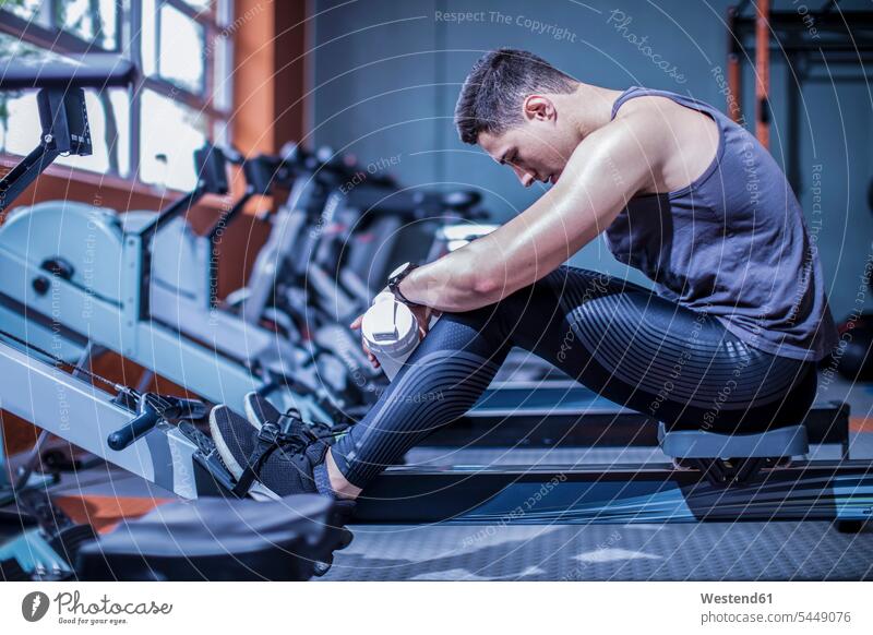 Junger Mann macht eine Pause am Rudergerät im Fitnessstudio trainieren Fitnessclubs Fitnessstudios Turnhalle Männer männlich fit Gesundheit gesund Sport