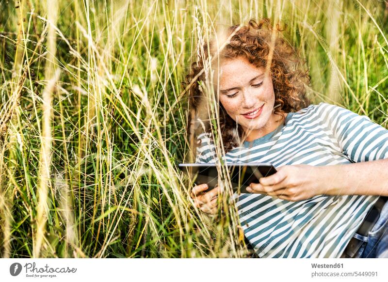 Lächelnde junge Frau entspannt sich auf einer Wiese mit Tablette weiblich Frauen Tablet Computer Tablet-PC Tablet PC iPad Tablet-Computer Erwachsener erwachsen