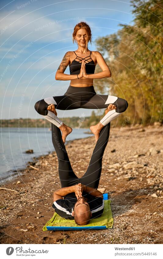 Akro-Yoga praktizierender junger Mann und Frau Akrobatik Acro Yoga balancieren Balance Trainieren Übung Üben Übungen Fuß Fuss Füße sitzen sitzend sitzt Fluss