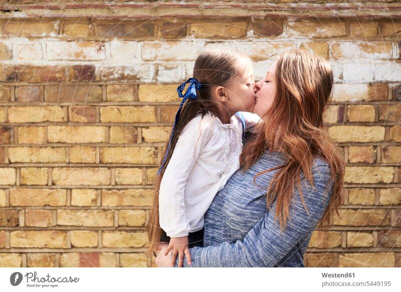 Mutter küsst ihre kleine Tochter vor einer Ziegelmauer Töchter küssen Küsse Kuss Mami Mutti Mütter Mama Kind Kinder Familie Familien Mensch Menschen Leute