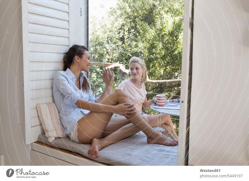 Zwei lächelnde junge Frauen durch Fensterscheibe getrennt Freundinnen weiblich entspannt entspanntheit relaxt sitzen sitzend sitzt Freunde Freundschaft