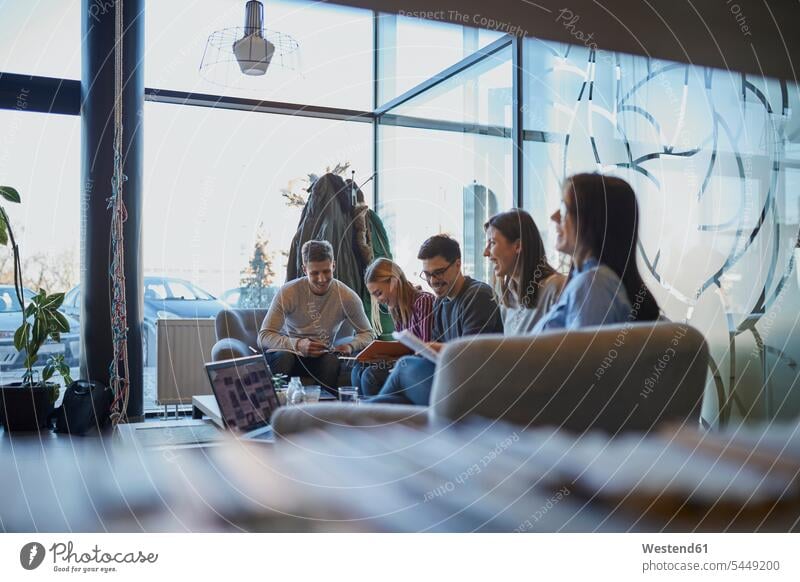 Gruppe glücklicher Freunde sitzt mit Laptop und Dokumenten in einem Café zusammen sitzen sitzend Cafe Kaffeehaus Bistro Cafes Cafés Kaffeehäuser Unterlagen