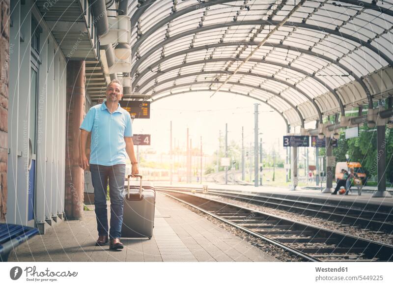 Lächelnder Mann mit Gepäck auf dem Bahnsteig Bahnhof Bahnhöfe Bahnhoefe Männer männlich Station Haltestelle Haltestellen Stationen Erwachsener erwachsen Mensch