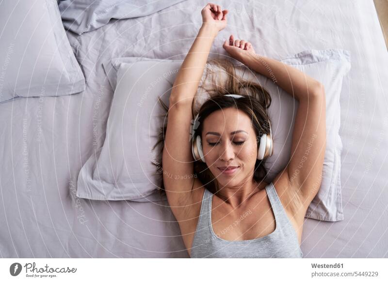 Entspannte Frau, die im Bett Musik hört hören hoeren entspannt entspanntheit relaxt Betten weiblich Frauen Entspannung relaxen entspannen Erwachsener erwachsen
