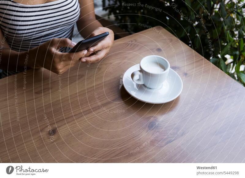 Junge Frau sitzt in einem Café und benutzt ein Mobiltelefon, Teilansicht Cafe Kaffeehaus Bistro Cafes Kaffeehäuser weiblich Frauen Erwachsener erwachsen Mensch