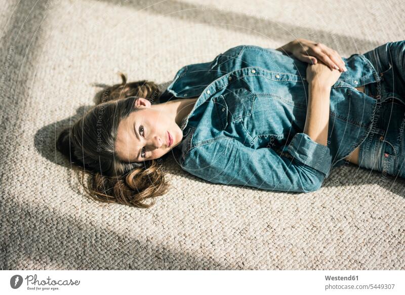 Porträt einer jungen Frau, die auf einem Teppich im Wohnzimmer liegt und das Sonnenlicht genießt liegen liegend Portrait Porträts Portraits weiblich Frauen
