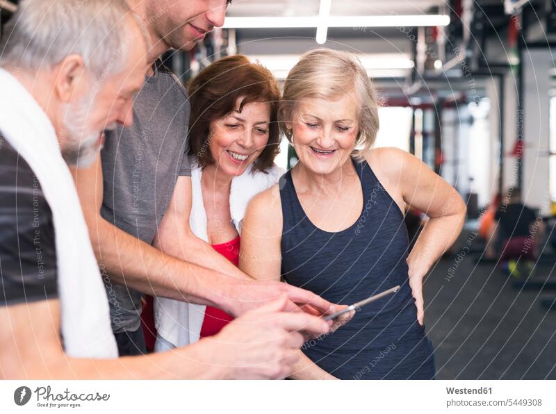 Gruppe von fitten Senioren und Personal Trainer im Fitnessstudio betrachtet Tablette Fitnessclubs Fitnessstudios Turnhalle ansehen Tablet Computer Tablet-PC