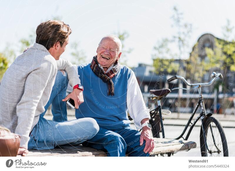 Lachender älterer Mann mit erwachsenem Enkel auf einer Bank glücklich Glück glücklich sein glücklichsein Großvater Opa Großpapa Großpapas Opas Opi Großväter