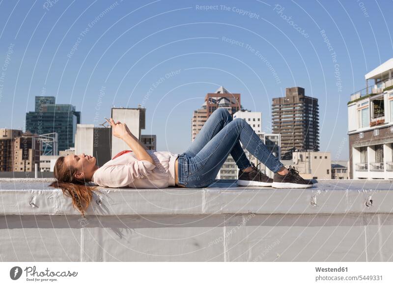 Junge Frau liegt auf der Balustrade einer Dachterrasse und benutzt ein Smartphone weiblich Frauen lesen Lektüre Brüstung blond blonde Haare blondes Haar
