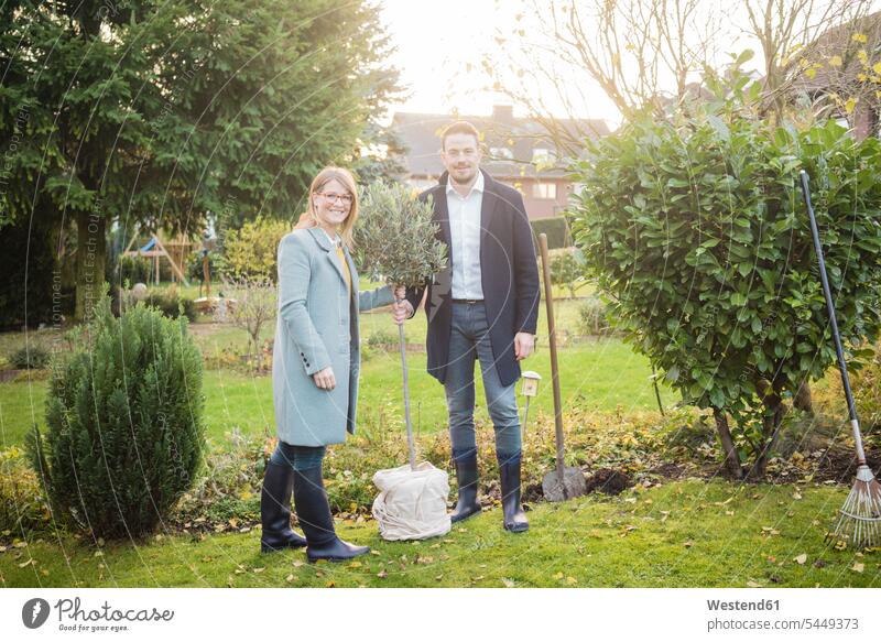 Porträt eines lächelnden Paares, das im Herbst im Garten steht und einen Baum pflanzt Portrait Porträts Portraits stehen stehend Gärten Gaerten einpflanzen