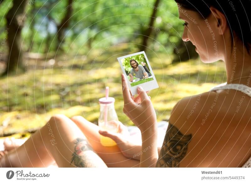 Junge Frau sitzt auf einer Decke im Wald und schaut auf ein Sofortbild sitzen sitzend Foto Fotos lächeln weiblich Frauen ansehen Bild Bildnis Bilder Erwachsener