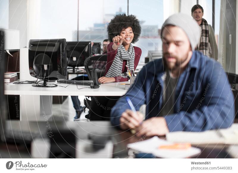 Lächelnde Frau am Schreibtisch im Büro, die auf einen Kollegen zeigt aufschreiben notieren Office Büros Arbeitsplatz Arbeitsstätte Arbeitstelle Arbeitstisch