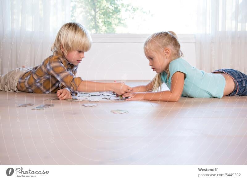 Bruder und Schwester liegen zu Hause auf dem Boden und spielen Puzzlespiele Brüder Böden Boeden Schwestern Zuhause daheim liegend liegt Geschwister Familie