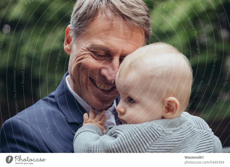Glücklicher reifer Geschäftsmann hält kleinen Jungen im Freien lächeln halten Vater Papas Väter Vati Vatis Papis Baby Babies Babys Säuglinge Kind Kinder