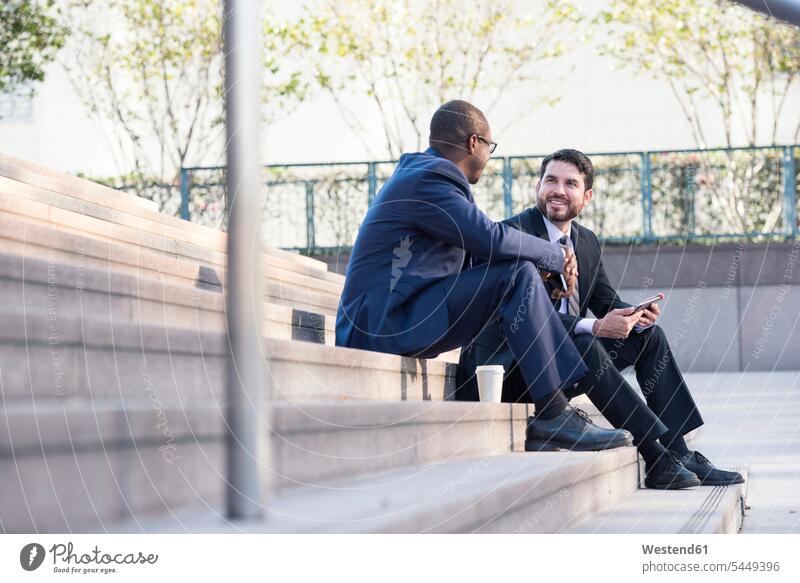 Zwei Geschäftsleute sitzen auf einer Treppe und unterhalten sich Treppenaufgang sprechen reden Geschäftsmann Businessmann Businessmänner Geschäftsmänner