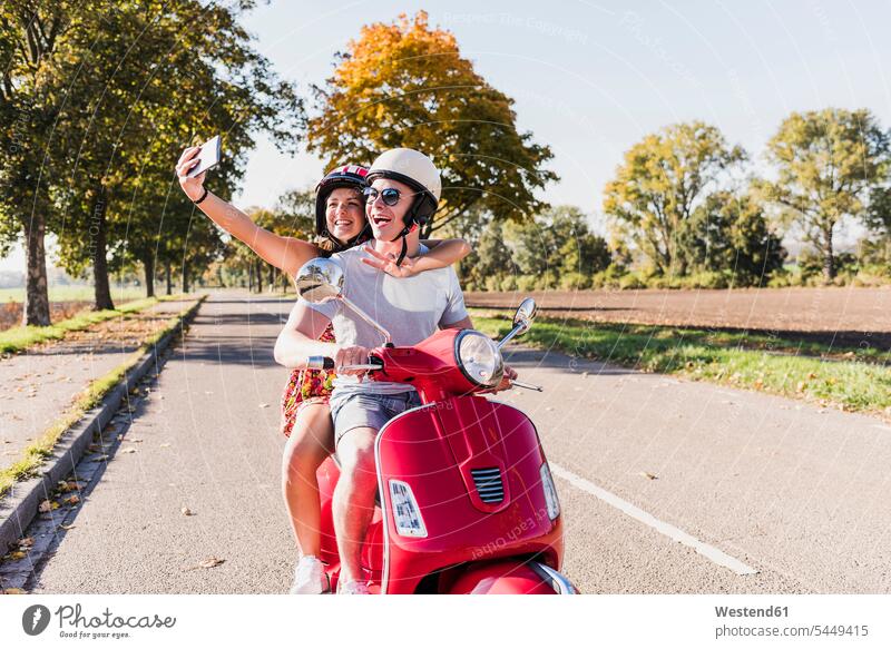 Glückliches junges Paar macht ein Selfie auf einem Motorroller auf einer Landstraße Selfies glücklich glücklich sein glücklichsein Landstraßen Pärchen Paare