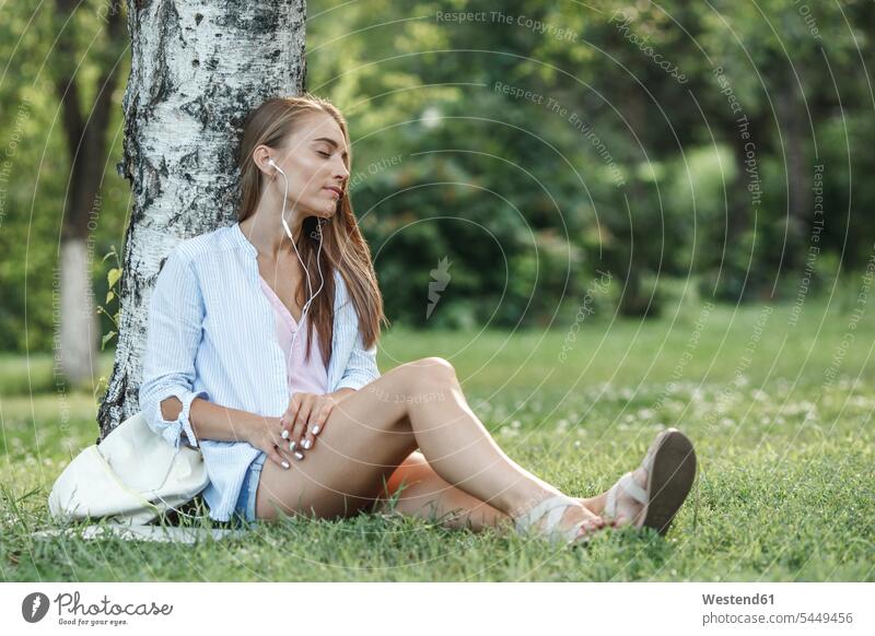 Junge Frau mit Kopfhörern entspannt sich auf einer Wiese Park Parkanlagen Parks Ohrhörer entspanntheit relaxt weiblich Frauen In-Ear Kopfhoerer Entspannung