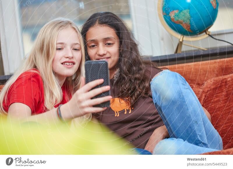 Zwei Mädchen auf der Couch teilen sich ein Smartphone lächeln weiblich Handy Mobiltelefon Handies Handys Mobiltelefone Sofa Couches Liege Sofas Freundinnen Kind