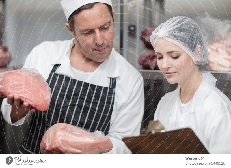 Mann und Frau mit Fleisch und Klemmbrett im Lagerhaus einer Metzgerei Fleischer Schlachter Schlaechter Schlächter Fleischhacker arbeiten Arbeit prüfen Kontrolle