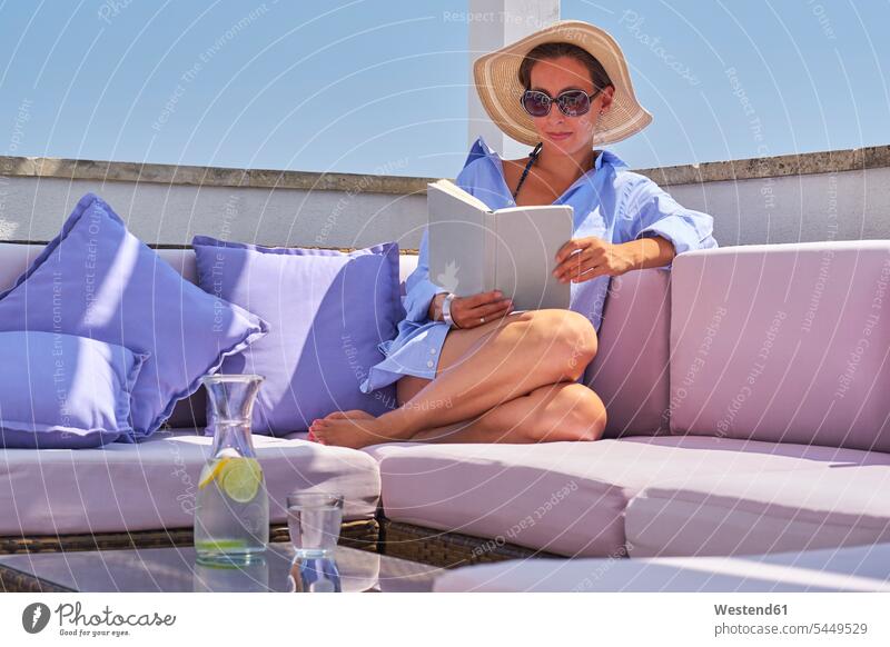 Frau mit Buch entspannt sich auf dem Sonnendeck Glas Trinkgläser Gläser Trinkglas Urlaub Ferien Wasser weiblich Frauen lesen Lektüre Entspannung relaxen