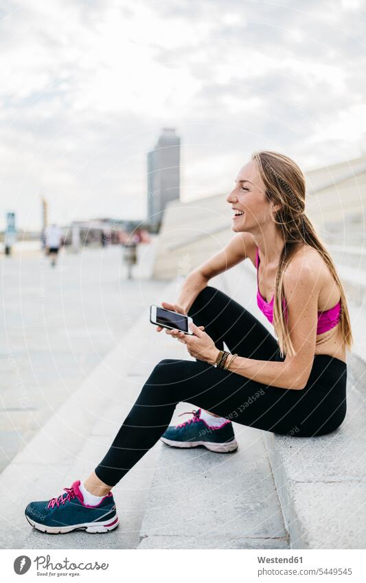 Junge Frau sitzt nach dem Training auf einer Treppe und benutzt ein Smartphone trainieren weiblich Frauen lachen Erwachsener erwachsen Mensch Menschen Leute