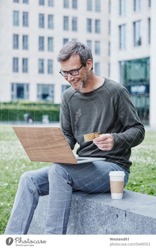 Reifer Mann im Freien mit Laptop, Kreditkarte und Kaffee zum Mitnehmen Portrait Porträts Portraits lächeln EC-Karte Kreditkarten Notebook Laptops Notebooks