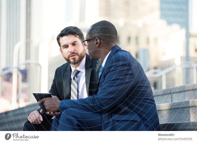 Zwei Geschäftsleute sitzen auf einer Treppe und unterhalten sich und teilen sich ein Tablett sprechen reden Geschäftsmann Businessmann Businessmänner