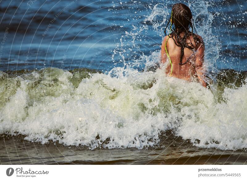 Kleines Mädchen spielt mit Wellen im Meer. Kind plantscht spielerisch mit Wellen. Kind springt in Meereswellen. Sommerurlaub am Strand Ferien MEER Spielen