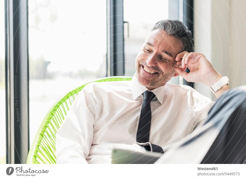 Porträt eines lachenden Geschäftsmannes, der in einem Sessel in seinem Büro sitzt Portrait Porträts Portraits Businessmann Businessmänner Geschäftsmänner