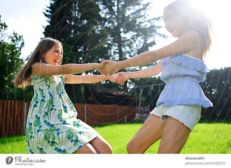 Zwei fröhlich verspielte Mädchen im Garten glücklich Glück glücklich sein glücklichsein weiblich spielen drehen Gärten Gaerten Freundinnen Kind Kinder Kids