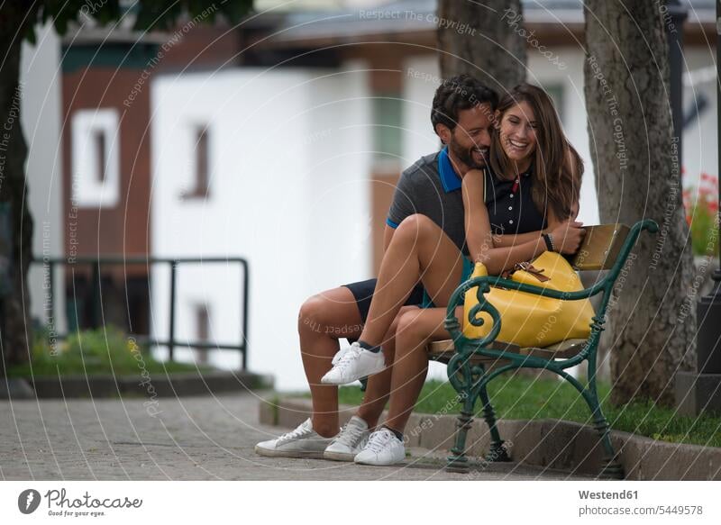 Glückliches Paar sitzt in einer Stadt auf einer Bank sitzen sitzend lachen Pärchen Paare Partnerschaft glücklich glücklich sein glücklichsein Sitzbänke Bänke