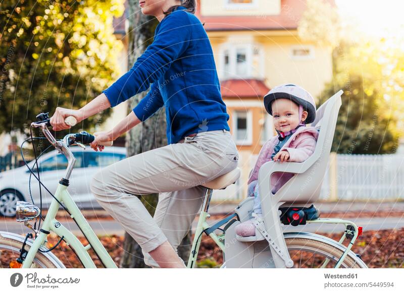 Mutter und Tochter fahren Fahrrad, das Baby trägt einen Helm und sitzt im Kindersitz Fahrradhelm Radhelm Fahrradhelme Bikes Fahrräder Räder radfahren
